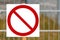 Forbidding sign, a white sign with a red crossed circle on the street against the background of a fence and grass. Signboard