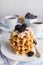 In the foreground is a blurred image of Belgian waffles with powdered sugar and blackberries, in the background are cups of coffee