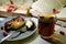 In the foreground is a gray plate of cheesecake and a fork and a piece of cake on it, a cup of tea and red viburnum berries