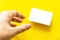 Foreground hand reaching empty white business card with shadow on yellow paper background