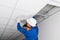 Foreman in blue uniform and white hard hat, installed a lighting lamp in the false ceiling