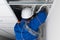 Foreman in blue uniform and white hard hat laying wiring for a Wi-Fi router in a hidden false ceiling system, close-up