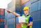 Foreman worker in hard hat and safety vest smiling and pointing control loading containers box from cargo