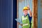 Foreman worker in hard hat and safety vest smiling and pointing control loading containers box from cargo