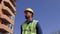 Foreman in a yellow helmet with a beard and mustache goes near the house under construction and tells about the construction proce