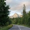 Forest asphalt road curve, coniferous trees and grass on both sides, mount Krivan peak symbol of Slovakia with sunset sky above