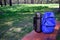 In the forest on the bench is a thermos and a blue backpack.