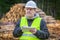 Forest engineer with tablet PC near piles of logs