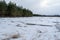 The forest lake is covered with snow-covered broken ice. Layers of cracked ice on a body of water. Early spring in a coniferous