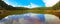 Forest lake of pine trees with a symmetric reflection of the trees and the cloudy sky in the water