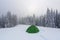 In the forest on the lawn green touristic tent stands with wide path to it. Amazing landscape on the cold winter day.