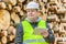 Forest Officer with tablet PC near pile of logs in forest