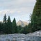 Forest river flowing, coniferous trees on both sides, mount Krivan peak Slovak symbol with summer evening clouds above in