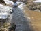 Forest river with glares on the surface in spring behind the snowdrifts.