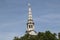 Forgotten church steeple between trees in London city. Historical monument from middle ages. Tower ends with a beautiful golden