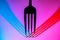 Fork with drops of water casting red blue shadows on white background. Fork tines close up. Silverware, stainless steel