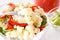 The fork holds a piece of cauliflower over a plate of fresh salad with cauliflower, tomatoes and greens