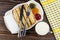 Fork and knife on dish with jams, pancake rolls, tissue, cup of milk, napkin on table. Top view