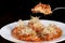 Fork picking up vegetarian ravioli with tomato sauce and sprouts of white dishes. black background