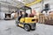 The forklift is old and scratched in a large and light warehouse. Yellow color