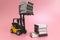 A forklift truck holds boxes of matches on a platform and loads them onto a stack from below. The concePink background. Copy space
