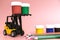 A forklift truck holds jars of gouache on a platform and loads them onto a stack from below. The concept of logistics and delivery