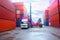 Forklift truck lifting cargo container in shipping yard or dock yard against sunrise sky with cargo container stack in background