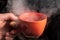 Fortune-telling on tea. Close-up sorcerer is hand holding a orang mug with steam on a dark background