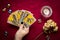 Fortuneteller's hand with black manicure lays out tarot cards, crystal, candle, dry roses on red tablecloth Flat lay Top view
