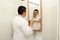 Forty-year-old Latino man brushes his teeth in the bathroom in a bathrobe looks in the mirror and takes care of his oral health