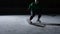 Forward in green uniform with stick in hands slides on ice and hitting puck. Man sliding on rink and cutting ice into