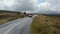 Forwards tracking of vintage sports car on road in highlands. Meadows and trees in forest around. Overcast sky. Ireland