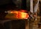 Foundry worker old blacksmith in protective clothing forming steel from orange molten metal. Forging glowing red hot iron