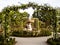 Fountain in the garden with arches covered in blossomed white roses