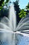 A fountain gushing water over a lake against a background of green trees.