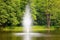 Fountain in the lake on a background of green, spring trees