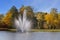 Fountain in a park lake.  Autumns trees and bushes  with yellow leaves