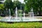 Fountain in summer city park, bright sunny day, trees with shadows and green grass