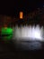 Fountains colored with light show and square section tower illuminated in orange at the background