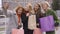 Four beautiful girlfriends posing on the street while one of them taking selfie. Four fashion women with shopping bags