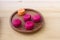 Four berry raspberry macaroons and the orange mango French macaroon on a wooden authentic plate on a wooden table.