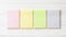 Four blank pastel yellow green pink reminder paper pad with horizontal line stripes on white pine wood