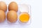 Four brown eggs lay on an egg tray with an eggshell on a white background. There was a broken egg, showing the yolk inside