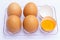 Four brown eggs lay on an egg tray with an eggshell on a white background. There was a broken egg, showing the yolk inside