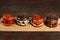 Four burgers on a light wooden board surface.