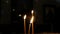 Four candles burning in the church in the dark against the background of people, slow motion