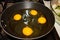 Four chicken eggs being cooked in a round black pan