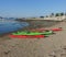 Four colorful sea kayaks lined up on a beach on a sunny day