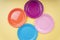 Four colourful plastic plate dishes over yellow beige background. Orange. Purple. Blue. Pink