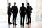 Four confident businessmen back in suit standing looking at window.